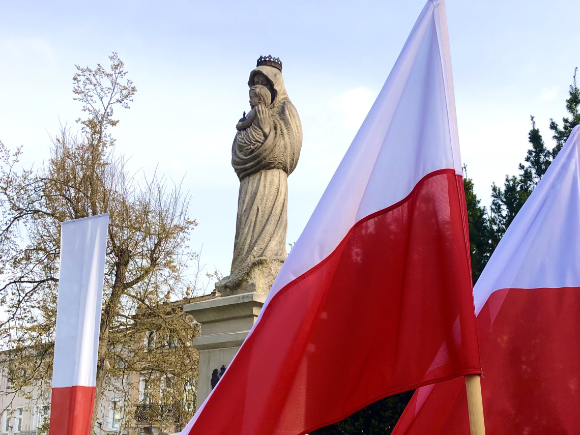 na zdjęciu widnieje flaga Polski oraz pomnik Matki Boskiej 